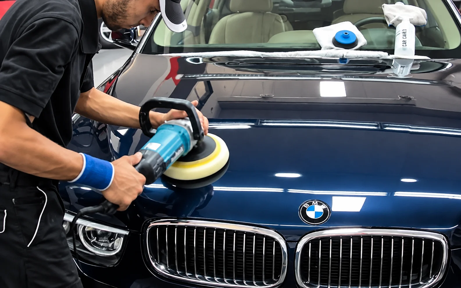 Technician polishing BMW car surface using machine inside workshop